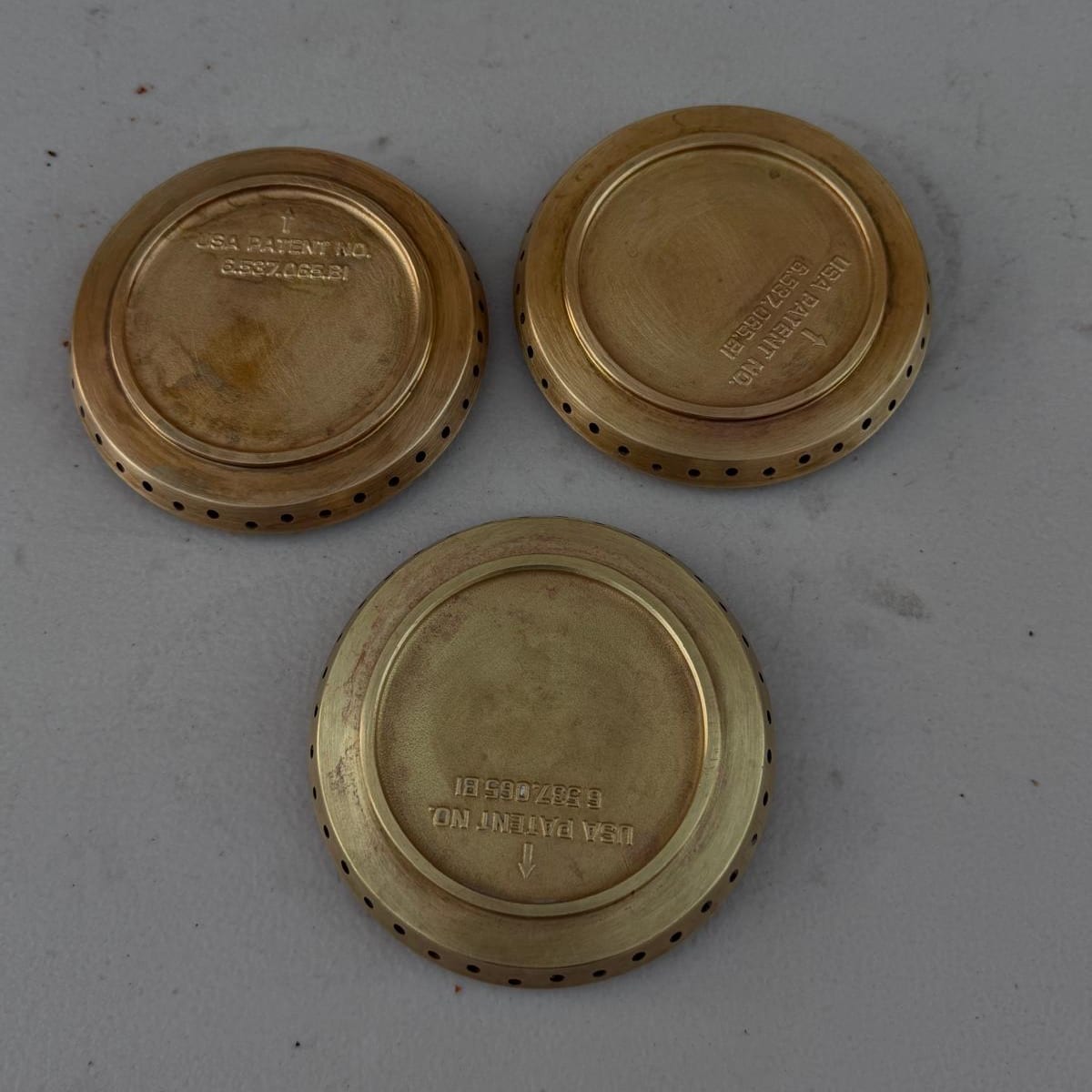 The same three Viking brass burner heads cleaned back to a bright brass finish, laid on a light surface in Newport Beach