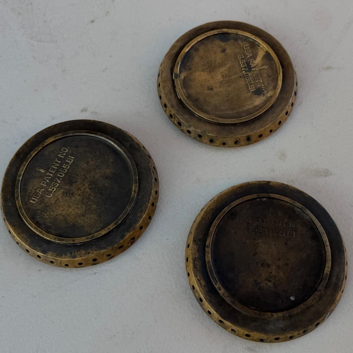 Three tarnished, darkened brass burner heads from a Viking range laid on a light surface before cleaning in Newport Beach