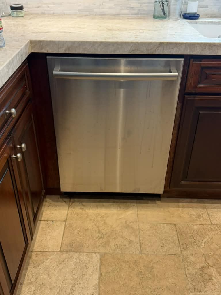 Closed stainless Bosch dishwasher under a beige countertop with brown cabinets in the same Laguna Beach kitchen