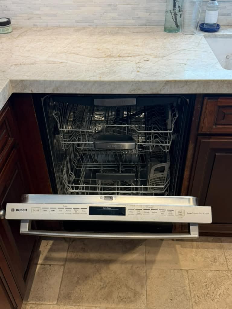 Open stainless Bosch dishwasher under a beige countertop with brown cabinets in a Laguna Beach kitchen