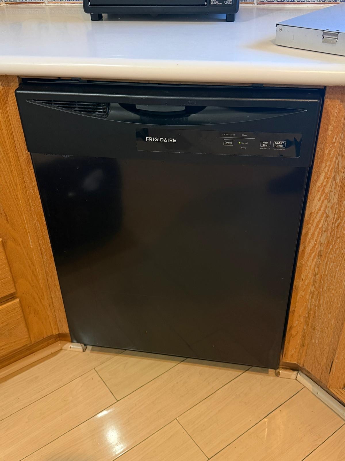 Black Frigidaire built-in dishwasher under a white countertop between oak cabinets in an Irvine kitchen