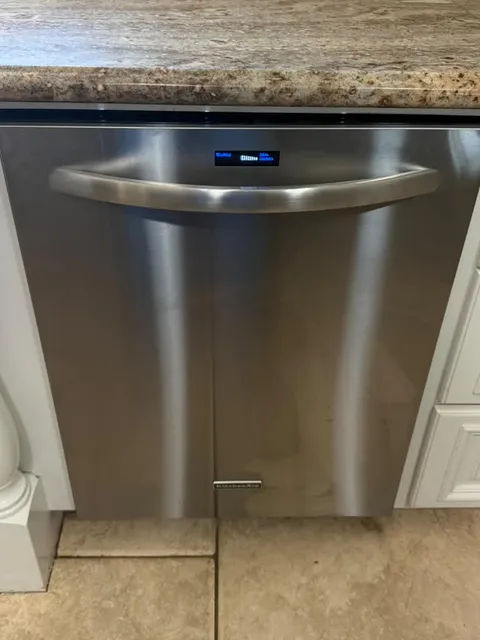 Stainless KitchenAid dishwasher with a lit display on its control panel, set under a countertop in a Santa Ana kitchen after a control board replacement