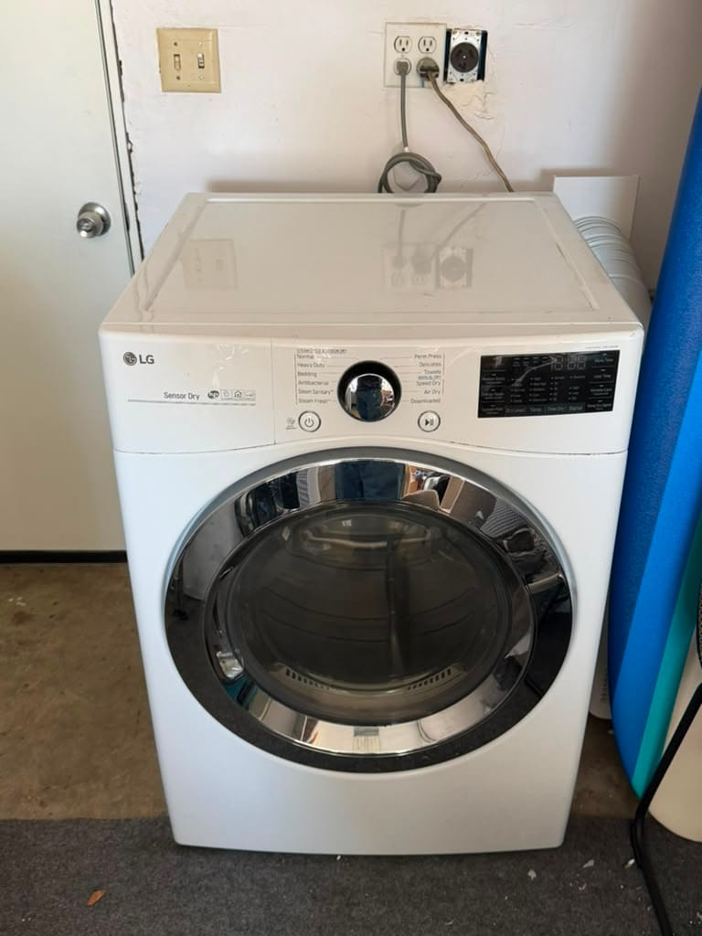 White LG front-load electric dryer standing in a Newport Beach garage laundry area, connected to its exhaust duct against the wall