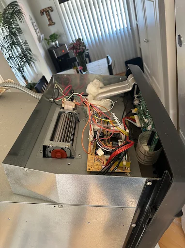 Open microwave chassis on a kitchen counter showing the fan assembly, circuit board, and wiring exposed for repair
