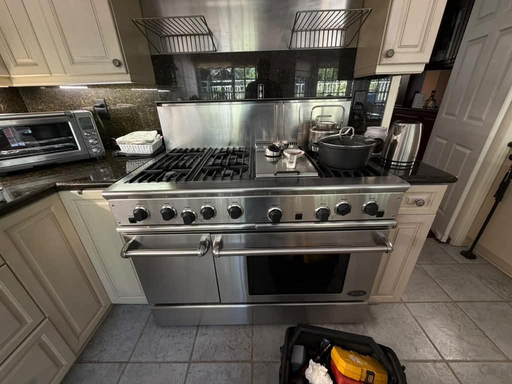 DCS range in an Orange, CA kitchen with all knobs on the control panel, a pot on a right-side burner and a tool bag on the floor