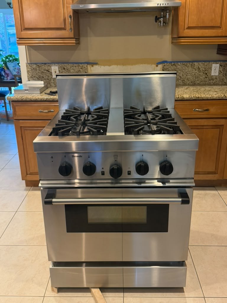 Stainless Thermador pro-style gas range pulled forward with its backguard raised, showing the star-shaped cast-iron burner grates, during a burner ignition repair in Orange, CA