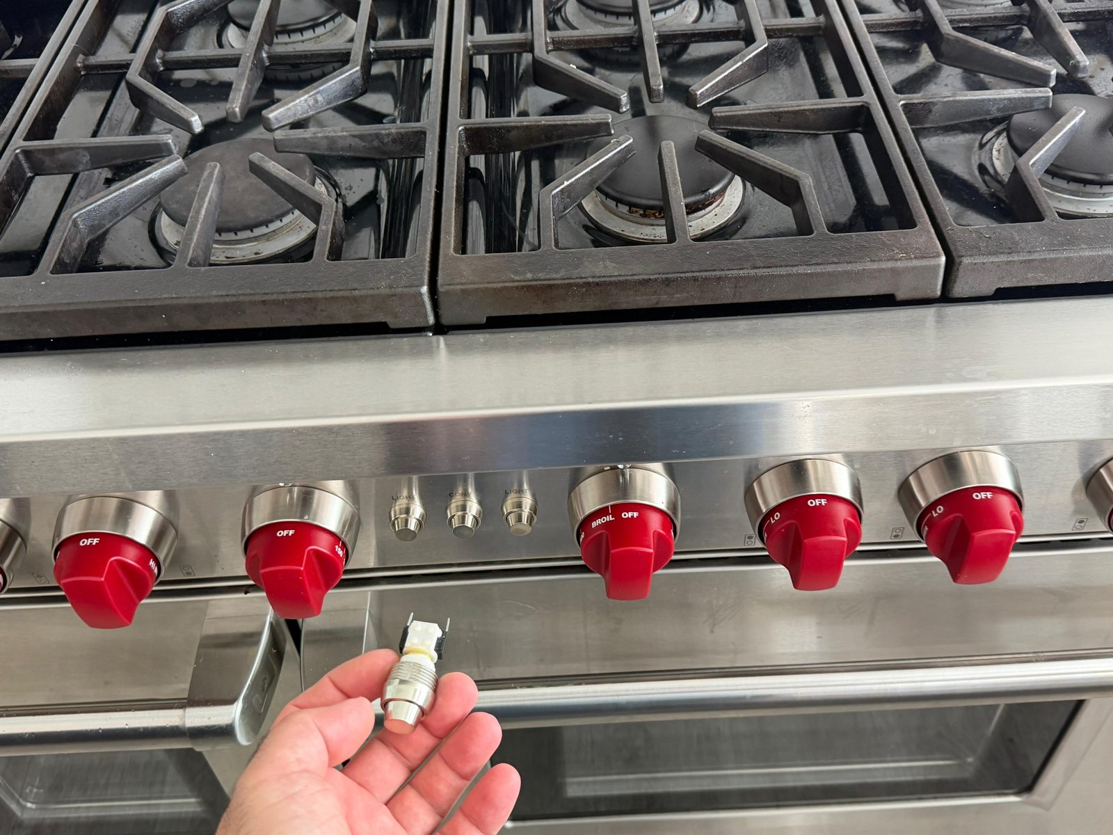 Technician holding the replaced convection fan on/off switch from a Wolf range during a Newport Beach service call