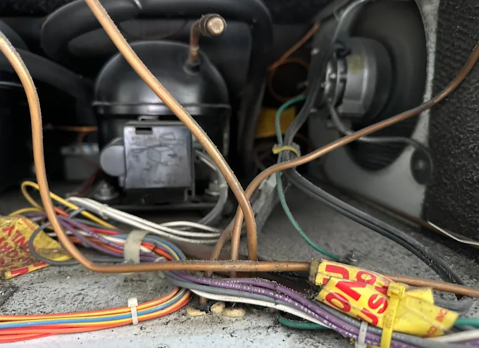 Close-up of a refrigerator's compressor compartment showing the compressor, copper tubing, and wiring harness