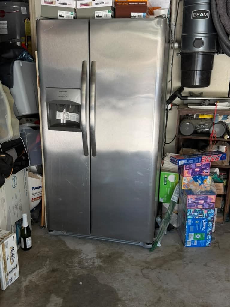 Stainless Frigidaire side-by-side refrigerator with a through-door ice and water dispenser, standing in a garage in Chino Hills