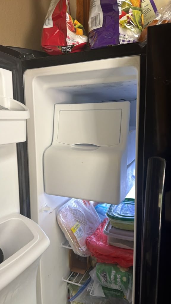Freezer compartment of a Frigidaire side-by-side refrigerator with the replacement ice maker assembly fitted to the freezer wall above the storage shelves