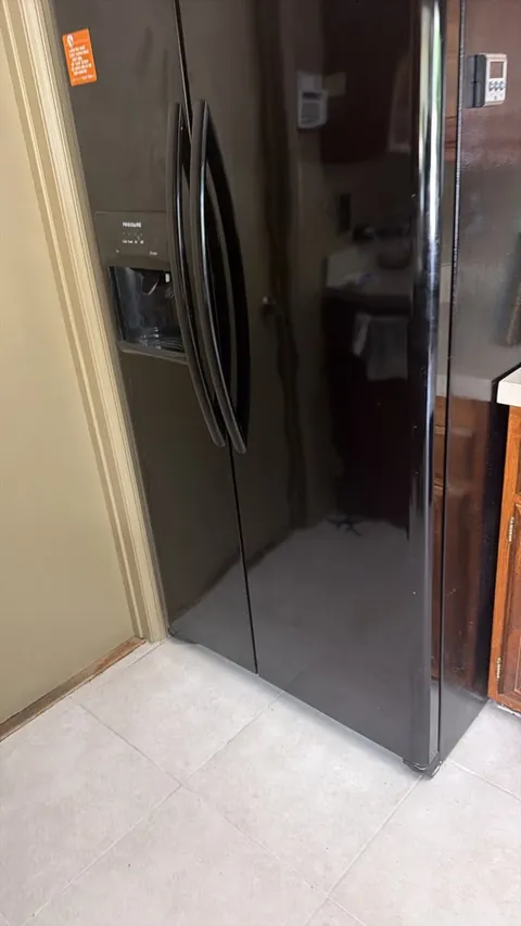 Black Frigidaire side-by-side refrigerator with a through-door ice and water dispenser, standing closed in a Mission Viejo kitchen after repair