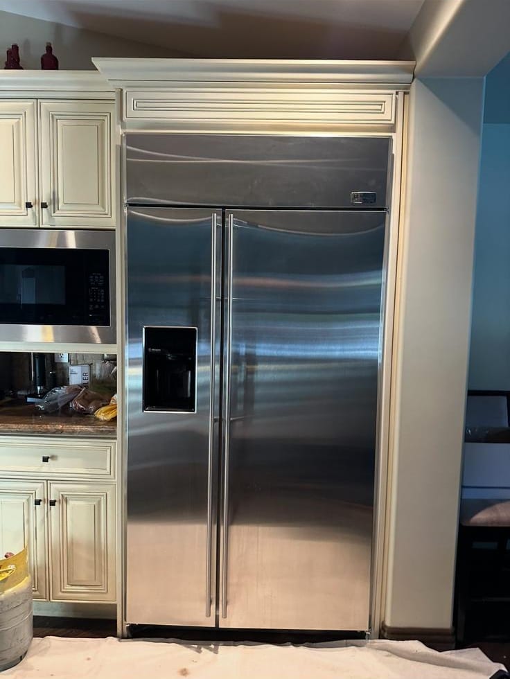 Stainless built-in Monogram refrigerator with straight handles and a door dispenser in cream cabinetry