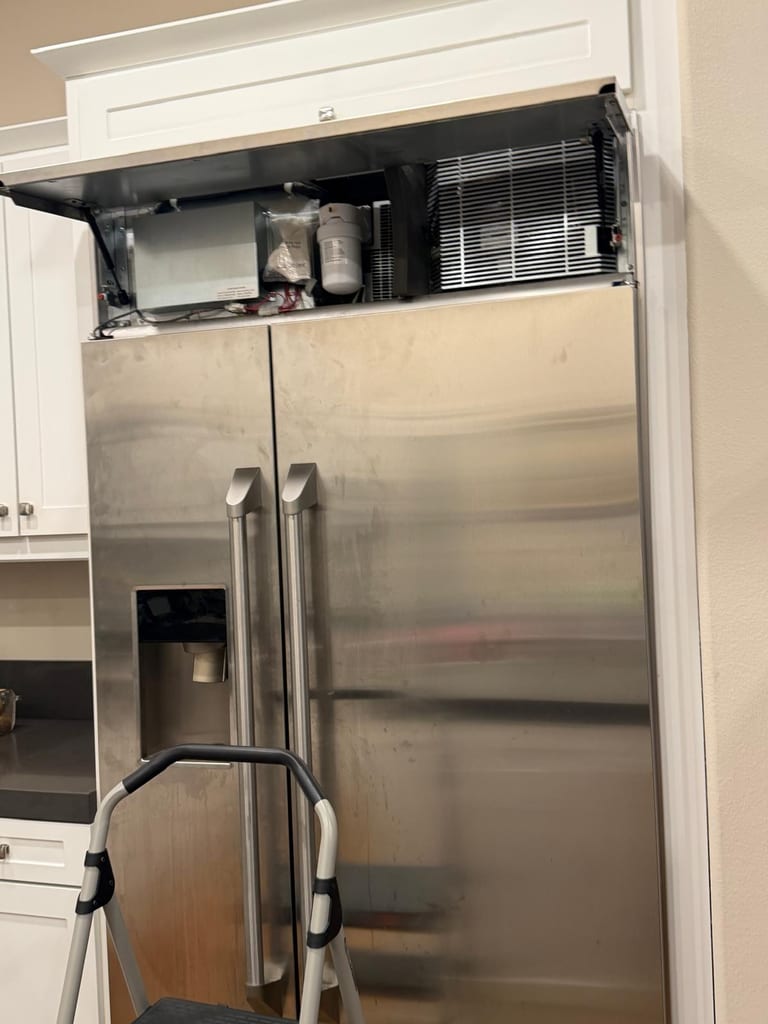 Stainless built-in GE Monogram side-by-side refrigerator with the upper service compartment open, exposing the water filter and wiring, in Irvine, CA