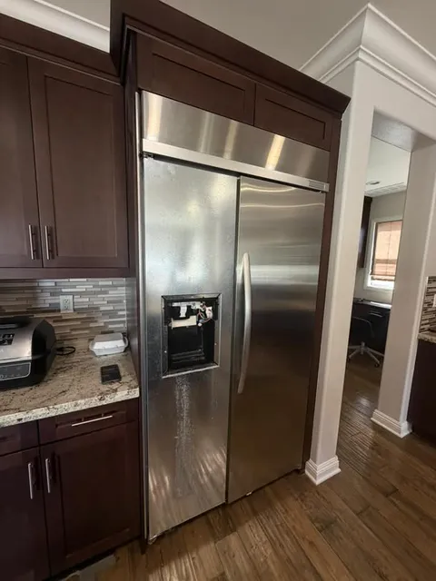 Stainless KitchenAid built-in side-by-side refrigerator with its water and ice dispenser panel removed, in a Brea kitchen during a water leak repair
