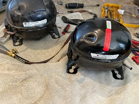 The failed LG FC75LBNA linear compressor next to the genuine FL80YLANA replacement on a workbench during an Orange, CA service call