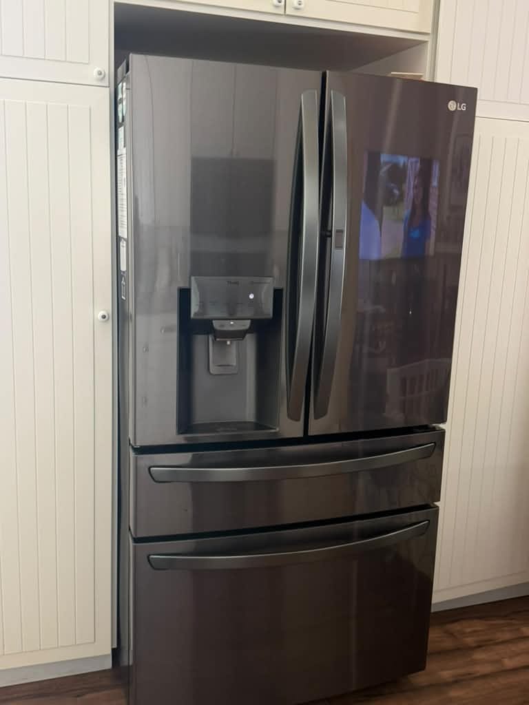 Black stainless LG French-door refrigerator with a door dispenser and two bottom drawers, set between white cabinets in a Mission Viejo kitchen