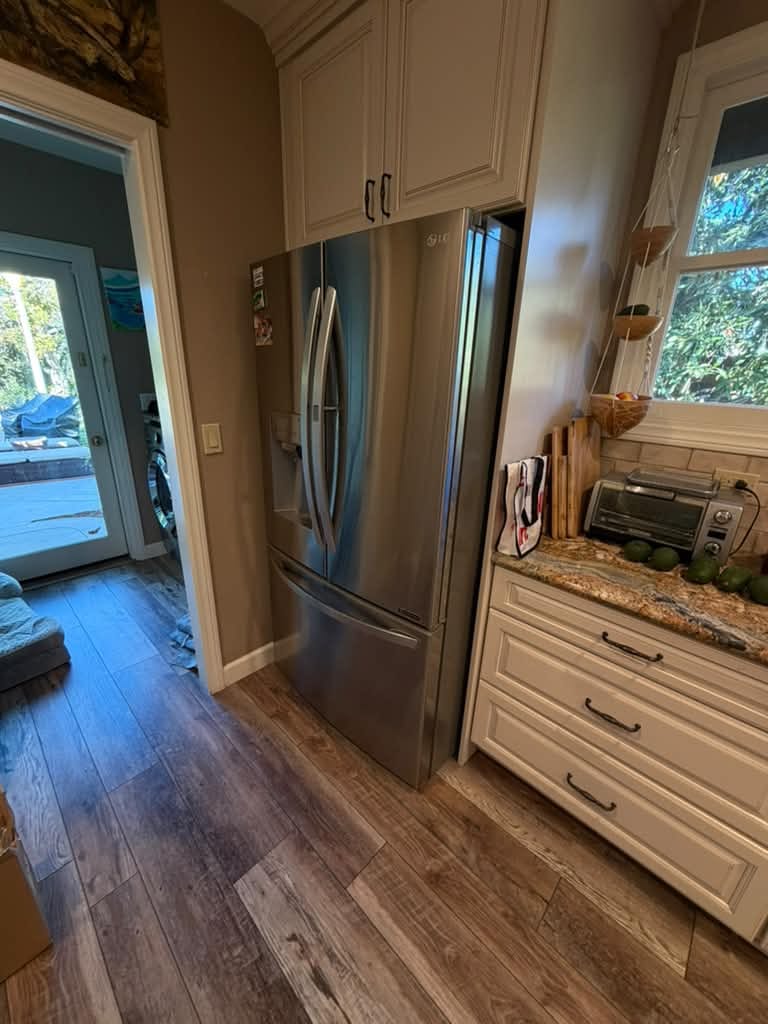 Stainless LG French-door refrigerator with a door dispenser, set into cream cabinets in an Orange, CA kitchen with a wood-look floor