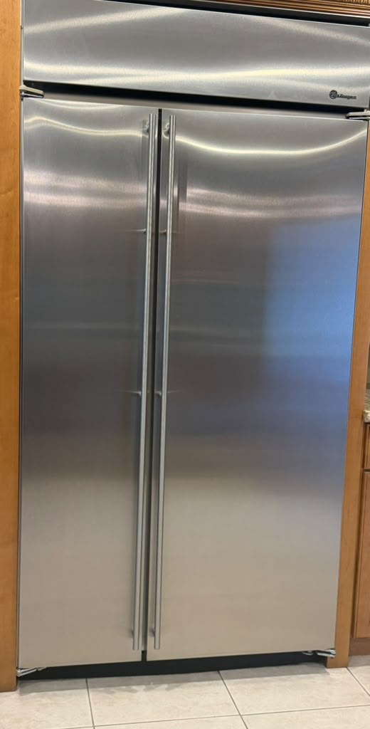 Stainless built-in GE Monogram side-by-side refrigerator fitted between oak cabinets in an Orange, CA kitchen after a water filter replacement and condenser coil cleaning