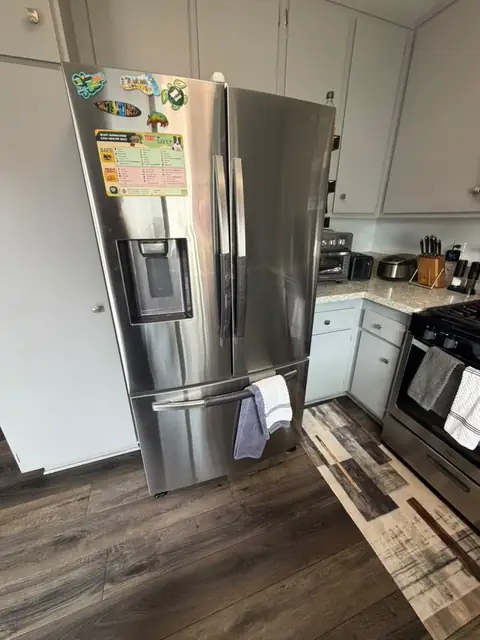 Stainless Samsung French-door refrigerator standing slightly forward of its cabinet alcove in a Garden Grove kitchen after a condenser coil cleaning
