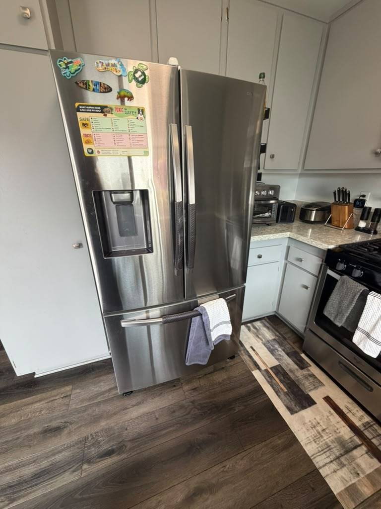 Stainless Samsung French-door refrigerator standing slightly forward of its cabinet alcove in a Garden Grove kitchen after a condenser coil cleaning
