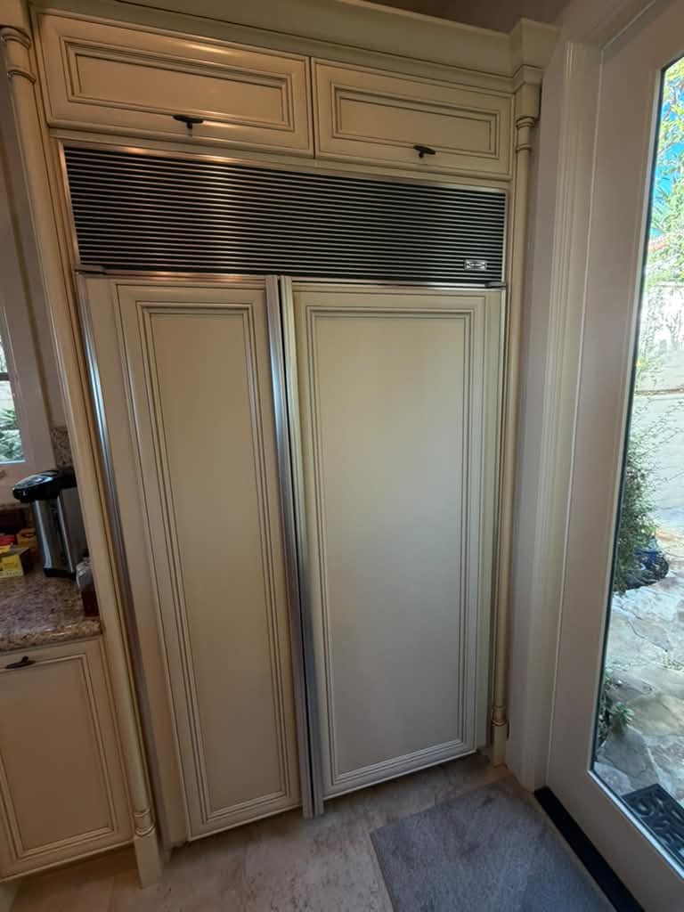Built-in Sub-Zero side-by-side refrigerator with cream custom door panels and a stainless top grille, Newport Beach
