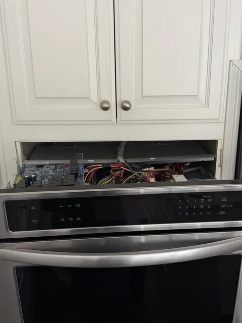 Stainless KitchenAid double wall oven with its control panel pulled forward to expose the control board, set in white cabinetry in a San Clemente kitchen