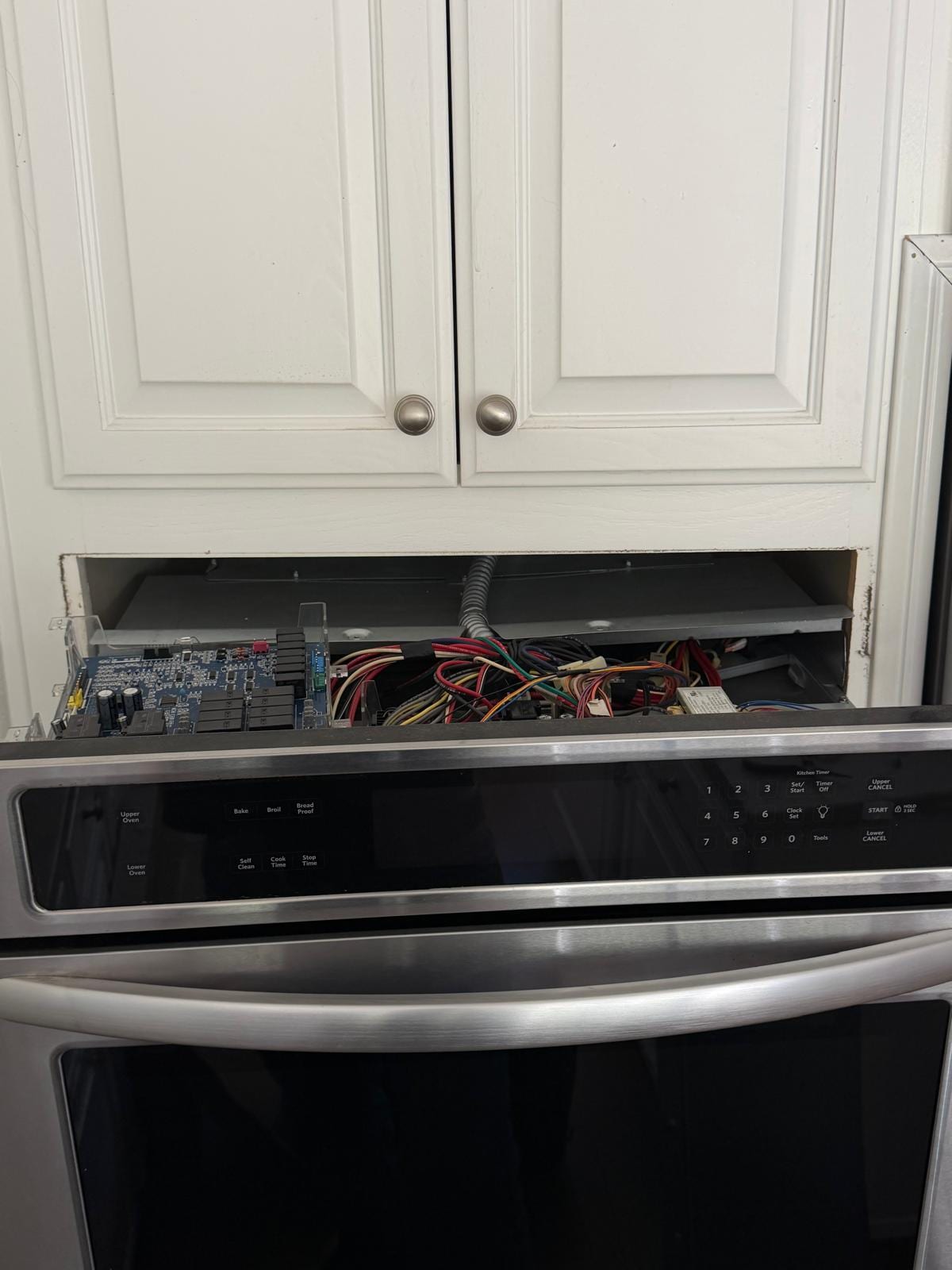 Stainless KitchenAid double wall oven with its control panel pulled forward to expose the control board, set in white cabinetry in a San Clemente kitchen