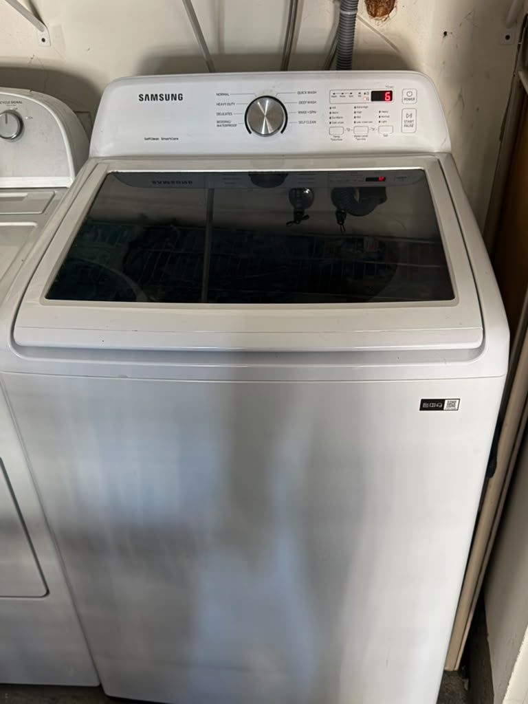 White Samsung top-load washer with a digital cycle panel, standing beside a white dryer in a Mission Viejo garage laundry area after a repair for violent shaking during the spin cycle