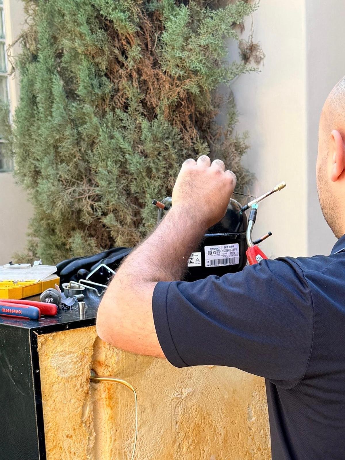 Universal Appliances Repair technician replacing the compressor on a Viking wine cooler in a Costa Mesa driveway