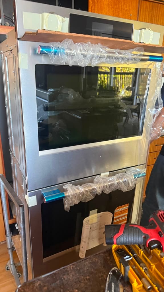 New KitchenAid double wall oven still in its protective wrap, raised on an appliance lift during installation in Tustin